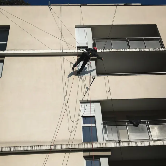 Cordiste suspendu contre la façade d'un immeuble moderne à balcons, vu depuis le bas