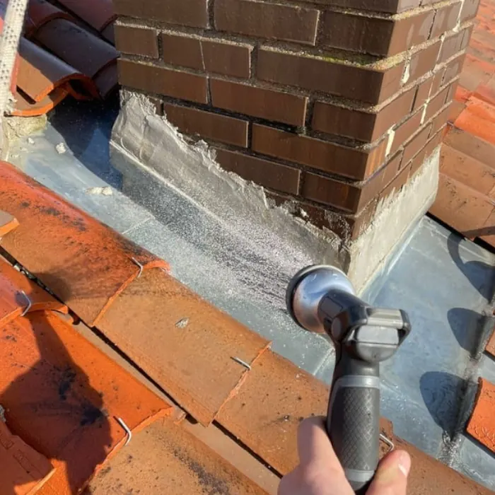 Soudure d'une bavette en zinc au pied d'une souche de cheminée en briques