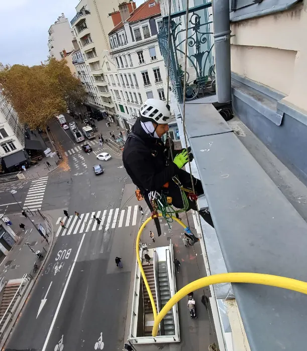 Cordiste casqué suspendu au-dessus d'une rue de centre-ville, tuyau d'eau à la main, le long d'une corniche